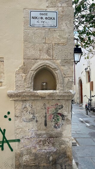 A stone structure with a sign, a small window, and graffiti. 3