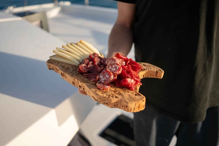 A wooden board with sliced cheeses and cured meats on a boat deck. 2