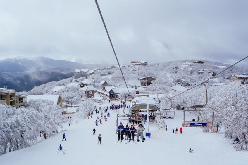 A snowy ski slope with a ski lift, buildings, and a mountain backdrop. 1