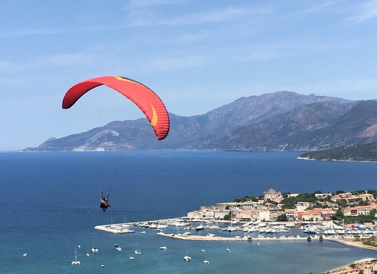A paraglider over a coastal town with boats and mountains in the background. 1
