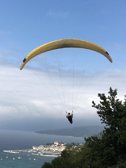 A paraglider with a yellow canopy flying over a coastal town. 2