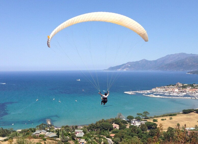 A paraglider over a coastal town with clear skies and a view of the sea and mountains. 5