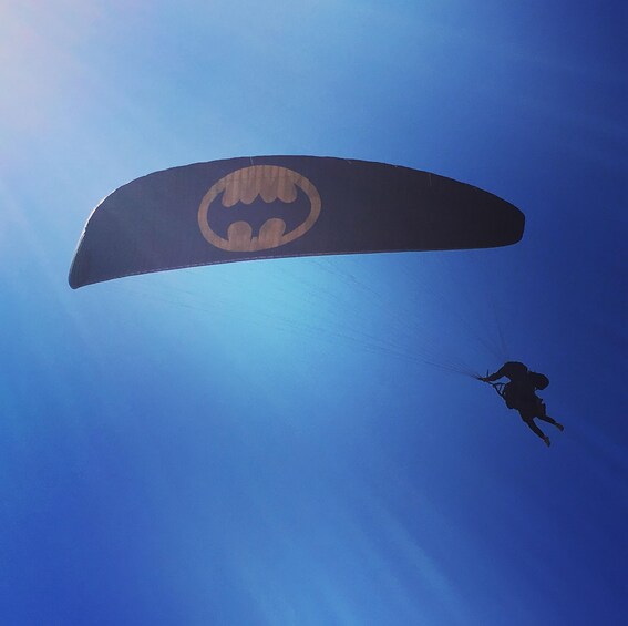 A parachute with a Batman logo, a person skydiving, and a clear blue sky. 3
