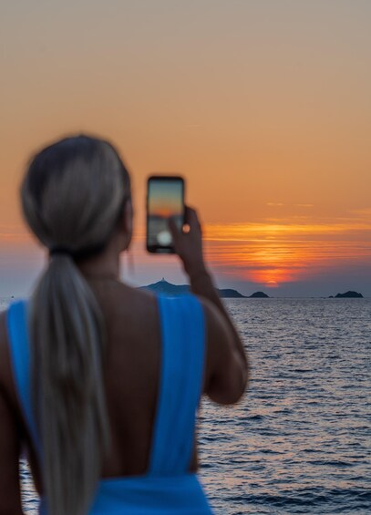 A person taking a photo of a sunset over the ocean with islands in the distance. 4