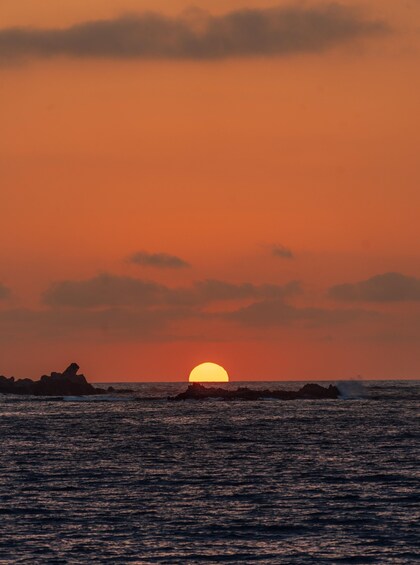 A sunset over the ocean with a silhouette of rocks in the foreground. 2