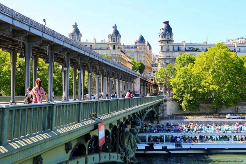 A green bridge with ornate railings, a river, and a boat with people on it. 4