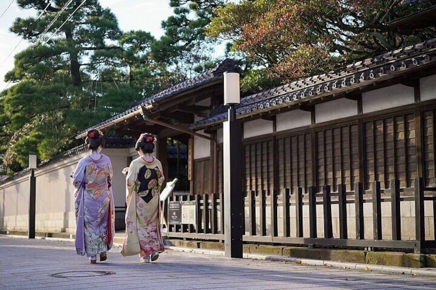 Two individuals in traditional Japanese attire walking along a pathway with a traditional Japanese building in the background. 3