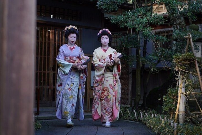 Two individuals in traditional Japanese attire standing in front of a wooden structure with a garden. 5