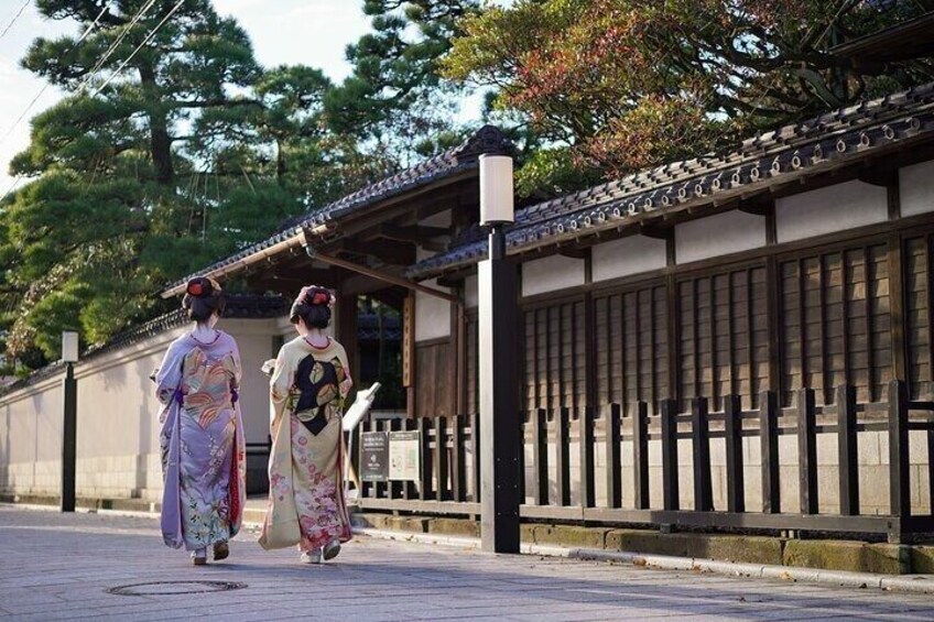 Two people in traditional Japanese attire walking along a pathway with a traditional building in the background. 3