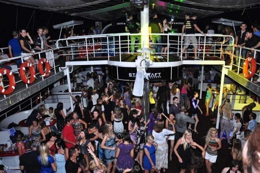A crowded indoor venue with a stage, railings, and a crowd of people. 4