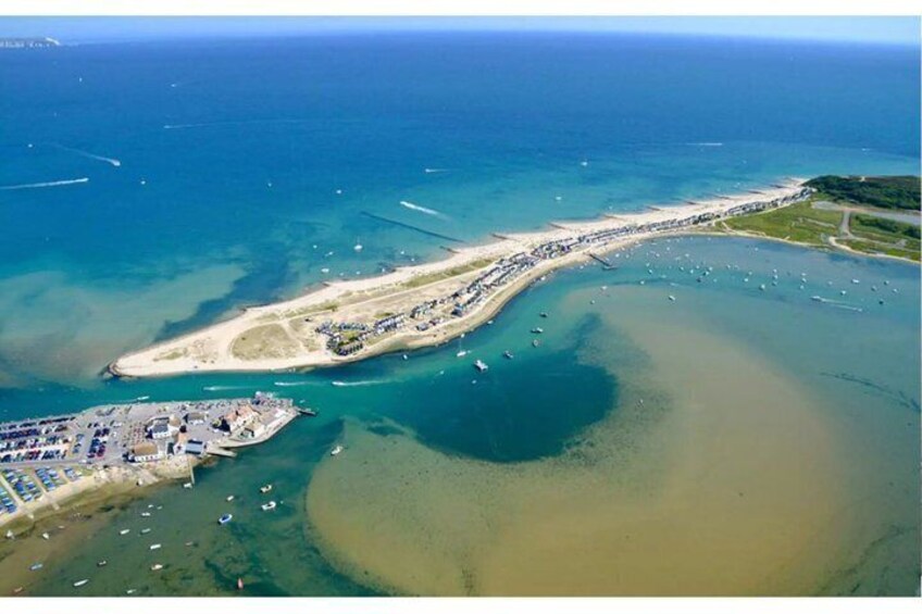 An aerial view of a coastal area with a long stretch of beach, a marina with boats, and a small peninsula with buildings. 4