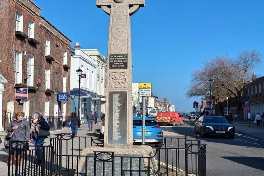 A stone monument with inscriptions, a street with pedestrians, and vehicles. 5