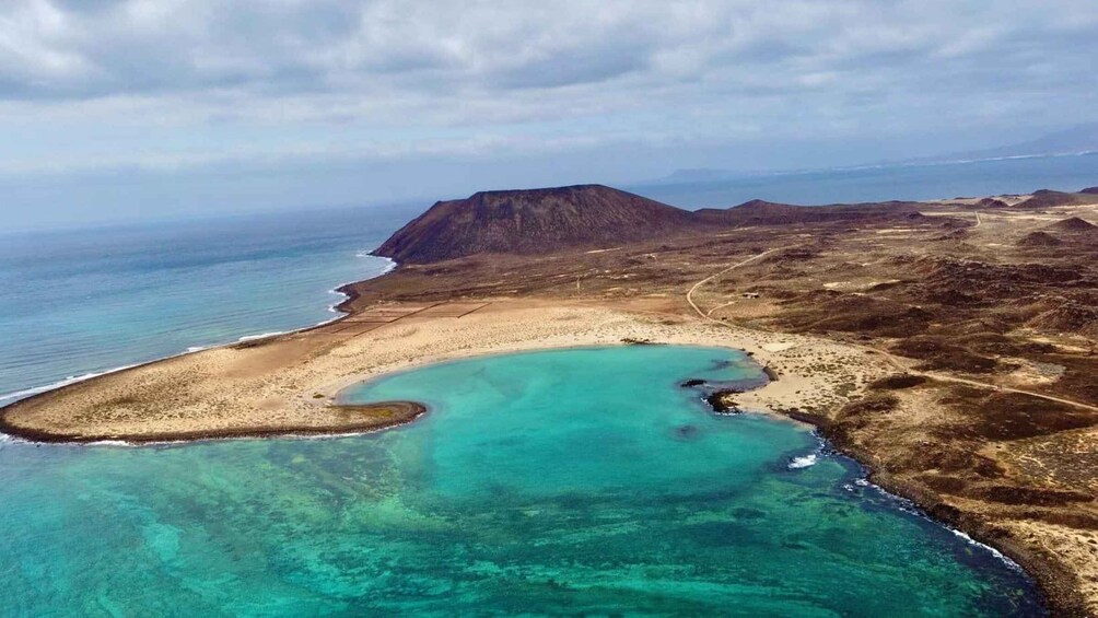 A coastal landscape with a clear turquoise bay, sandy beach, and a mountain in the distance. 2