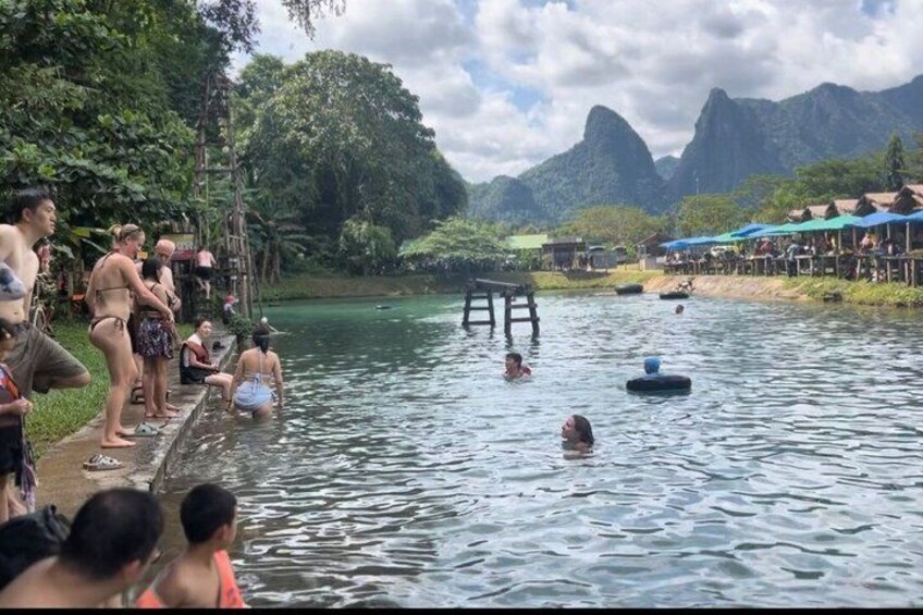 People swimming and floating on a river with a forested landscape and mountains in the background. 2