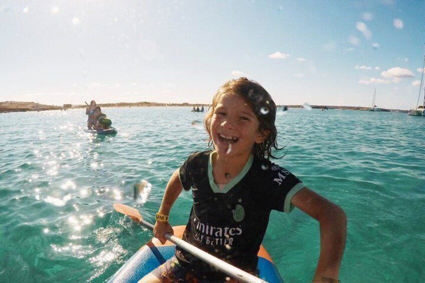 A person on a paddleboard in clear blue water with a distant shoreline and sailboats. 1