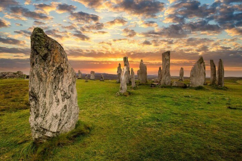 A stone circle with a large central stone and smaller stones arranged around it, set against a sunset sky. 1