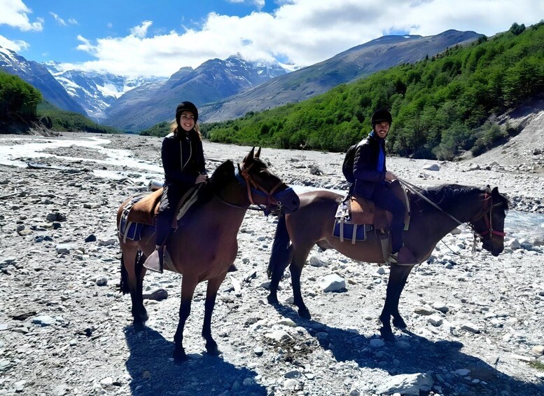 Two people riding horses on a rocky terrain with mountains in the background. 5