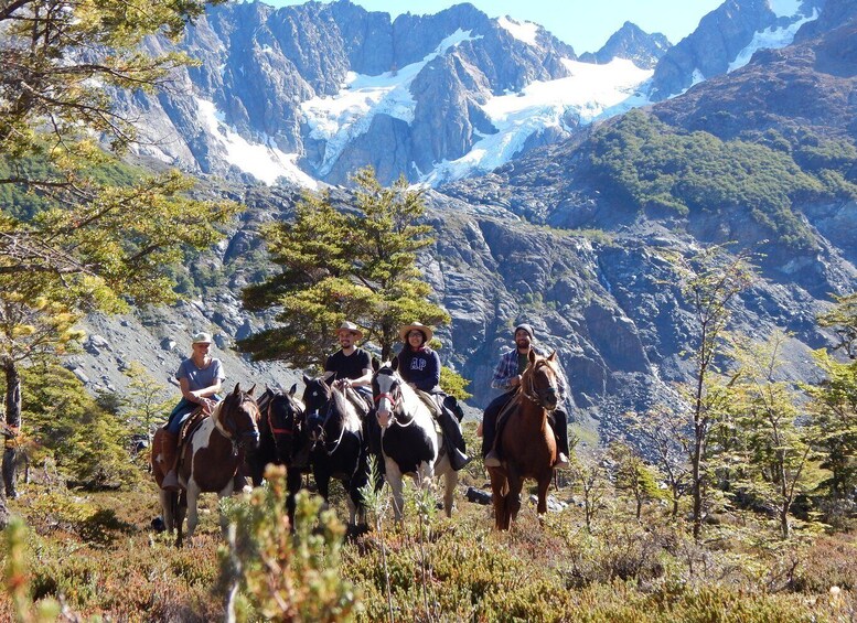 A group of people riding horses on a mountain trail with snow-capped peaks in the background. 3