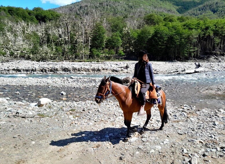 A person riding a horse by a river with a mountainous backdrop. 2