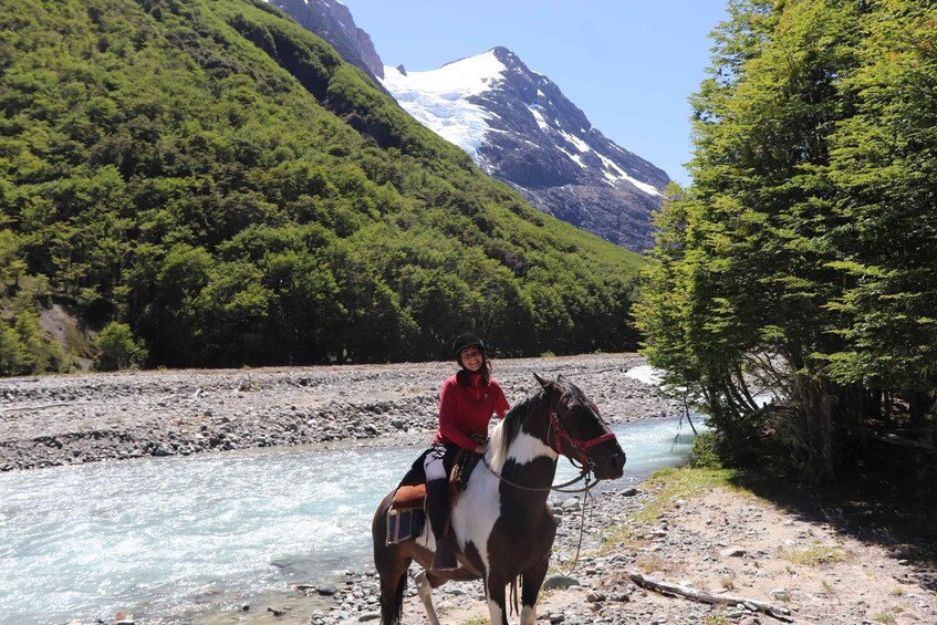 A person riding a horse by a river with a mountain in the background. 1