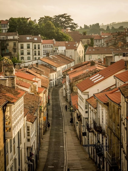 A narrow street lined with historic buildings, a few pedestrians, and trees in the background. 4