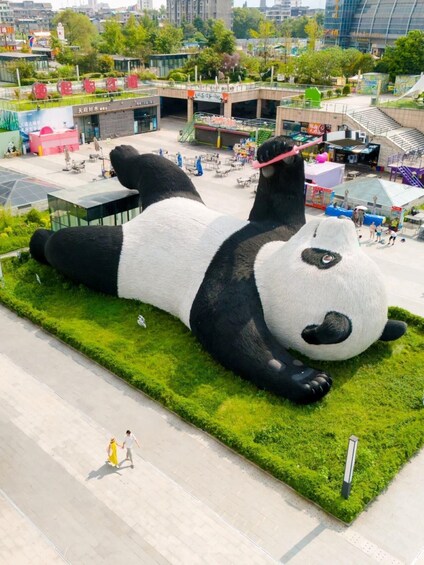 A large panda sculpture lying on a grassy area with a cityscape in the background. 1