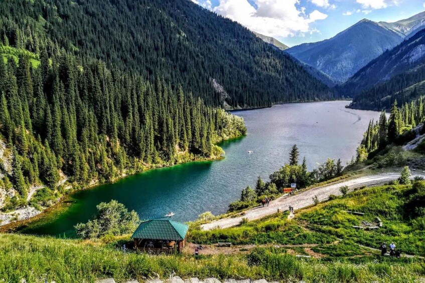 A lake surrounded by dense forest and mountains, with a small cabin and a trail leading to it. 4