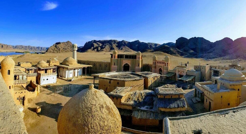 A desert town with traditional architecture, including domed buildings and a mosque with a minaret. 1