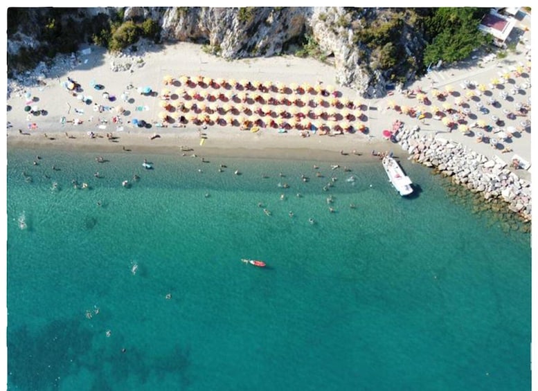 An aerial view of a beach with people swimming and sunbathing, umbrellas, and a boat. 5