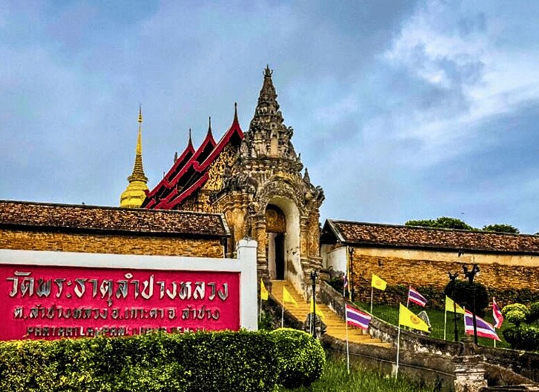 A traditional Thai temple with a golden spire, a red-roofed entrance, and a sign in a foreign language. 2