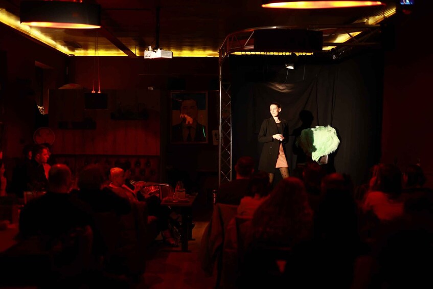 A dimly lit room with a stage, a microphone stand, and a person standing on stage. 2