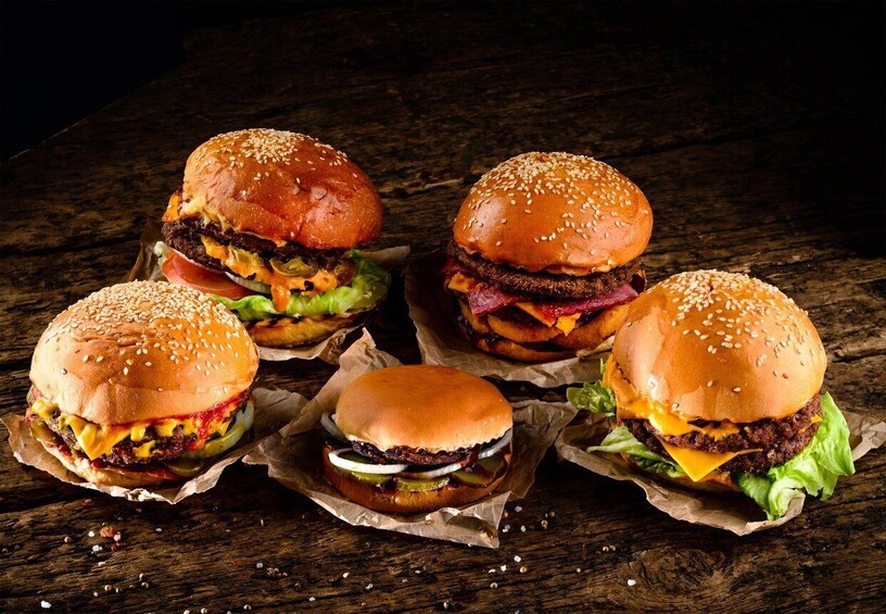 Four burgers with sesame seed buns, lettuce, cheese, and beef patties on a wooden surface. 3