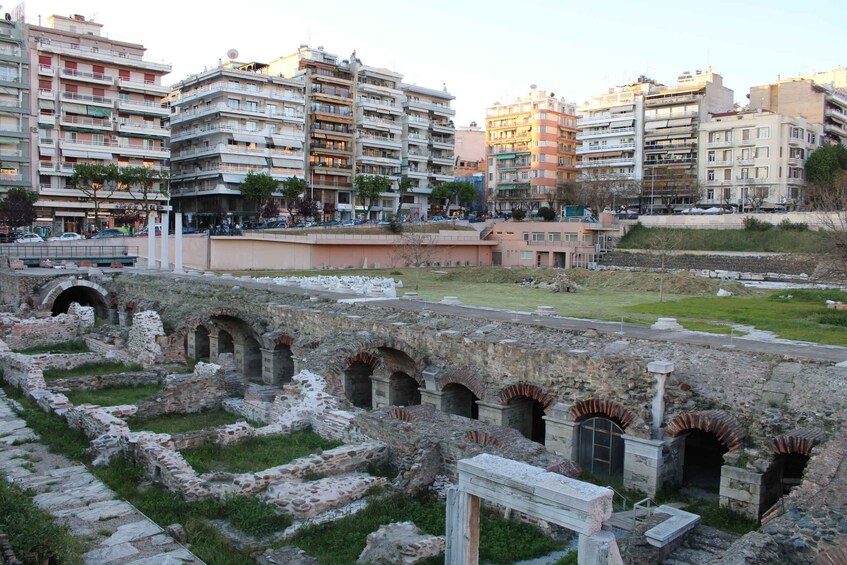 Ancient ruins with arches and columns, surrounded by modern buildings and a grassy area. 3