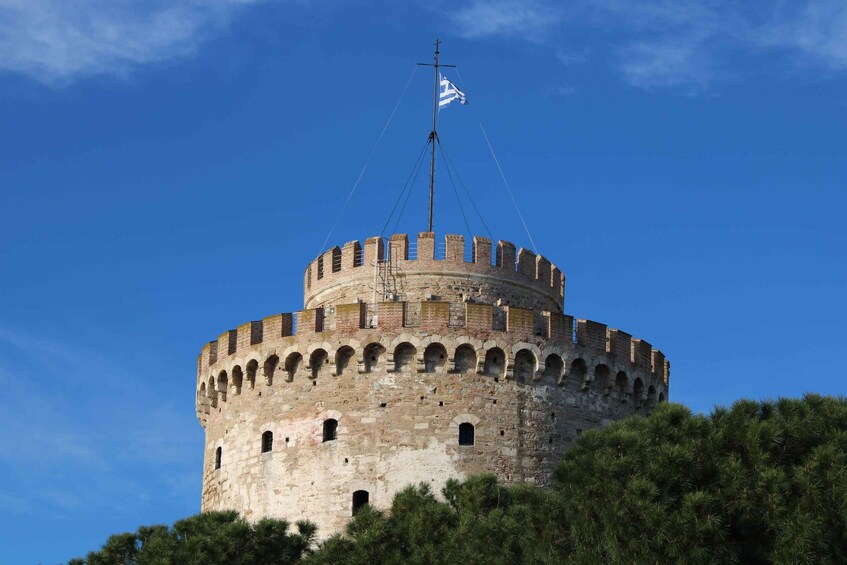 A historic stone tower with a flag atop, surrounded by greenery. 1