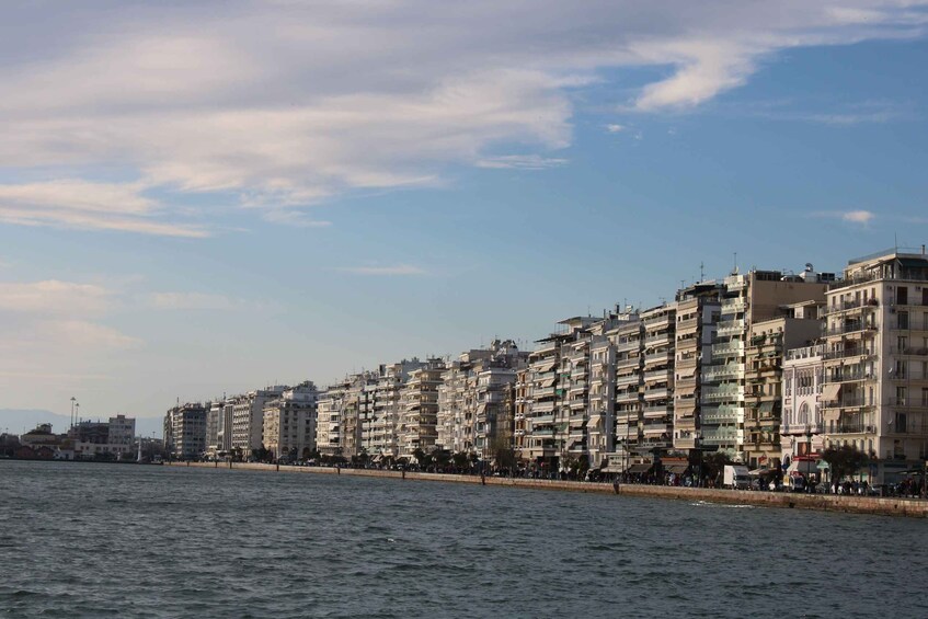 A waterfront cityscape with multi-story buildings, a calm sea, and a clear sky. 2