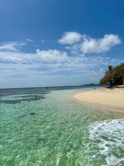 A beach with clear turquoise water, a sandy shore, and a distant person walking. 2