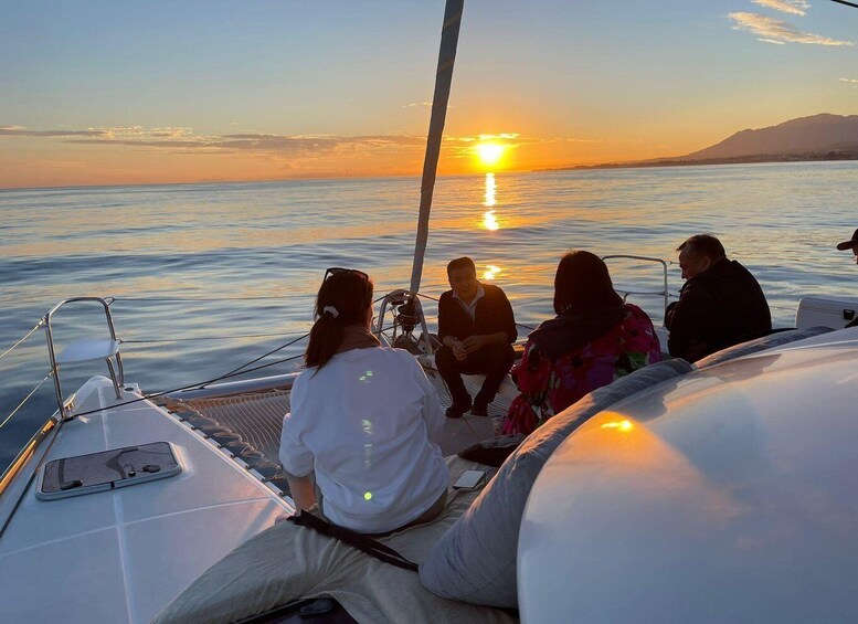 A group of people on a sailboat at sunset with calm waters and a distant mountain range. 2