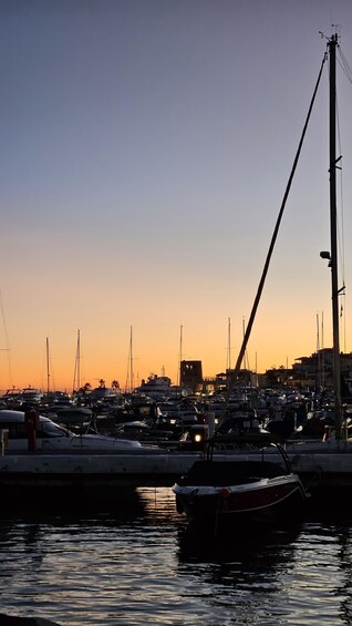A marina at sunset with boats docked, a crane, and buildings in the background. 4