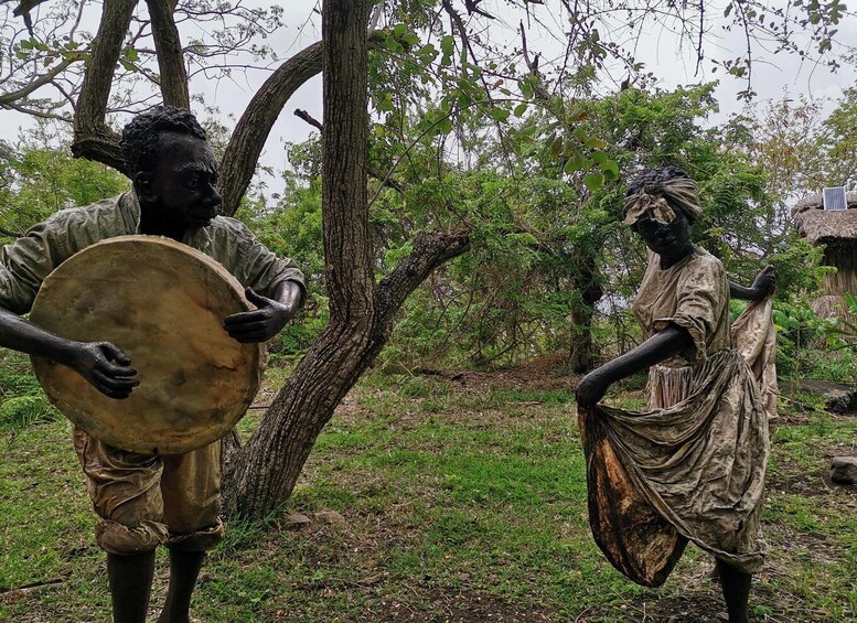 Two statues of African figures, one holding a drum, set against a backdrop of trees and grass. 5