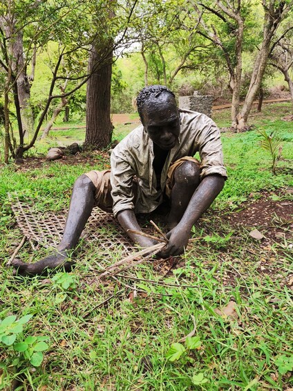A statue of a person sitting on the ground surrounded by greenery. 2