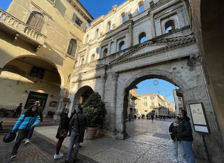 A historic archway with people walking through it, a cafe, and a building with a balcony. 4