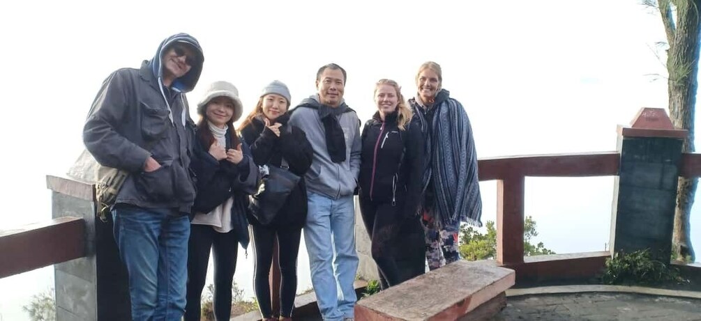 A group of people standing on a wooden deck with a railing, overlooking a body of water. 5