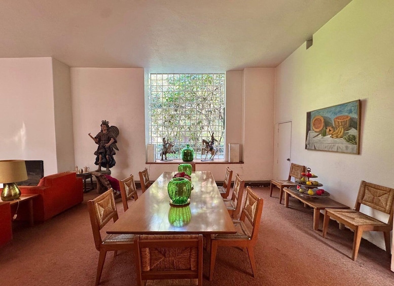 A dining room with a wooden table, chairs, a red sofa, a statue, a window with a view, and a painting on the wall. 4