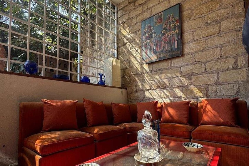 A room with a brown leather sofa, a glass coffee table, and a painting on a stone wall. 1
