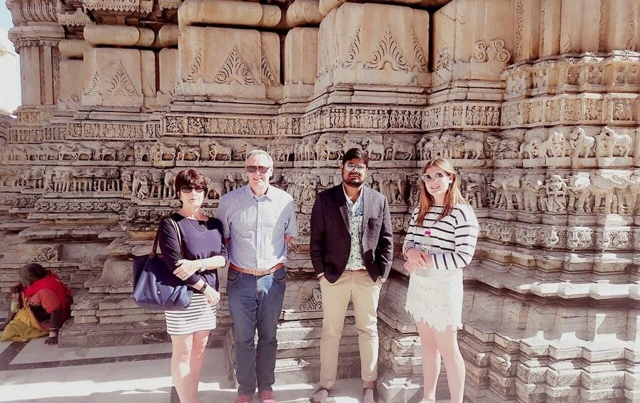 A group of people standing in front of a detailed stone structure with carvings. 3