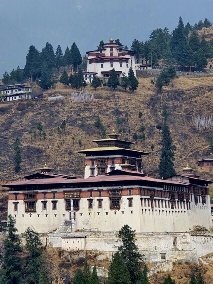 A large white building with a red roof, surrounded by trees and hills. 2