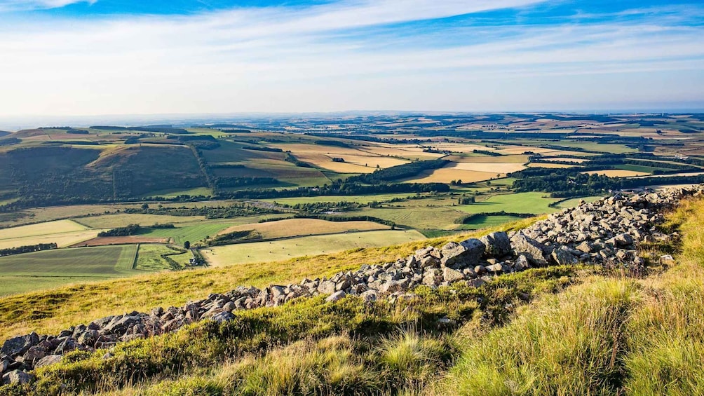A panoramic view of a rural landscape with rolling hills, fields, and a stone wall in the foreground. 3