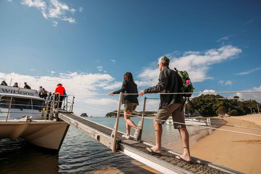 People crossing a bridge to a boat named 'Wilsons' with a clear sky and calm sea. 3