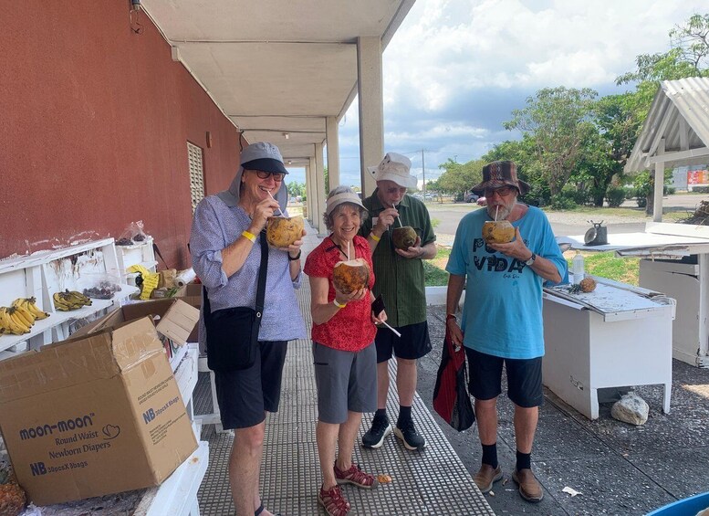 A group of people outdoors near a building with a covered area, some holding coconuts. 5