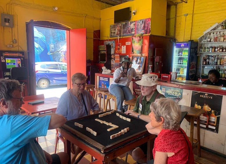 A group of people playing mahjong at a bar with a car parked outside. 1